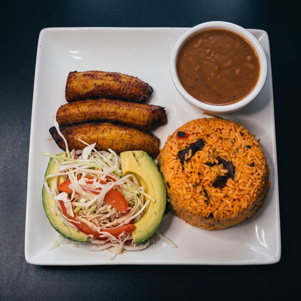 Fried plantains, red rice, avocado salad, and a bowl of beans on a white plate.