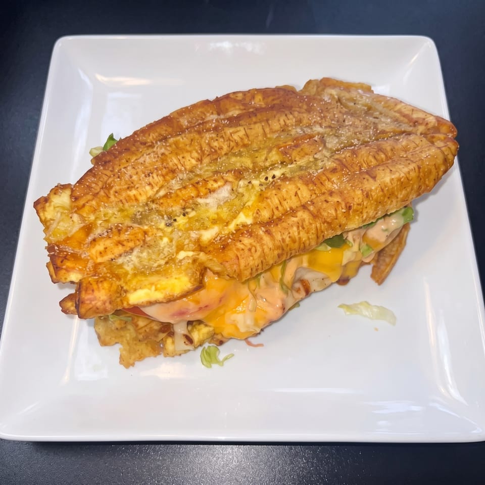 Golden plantain sandwich filled with melted cheese, sauce, and lettuce on a white plate.