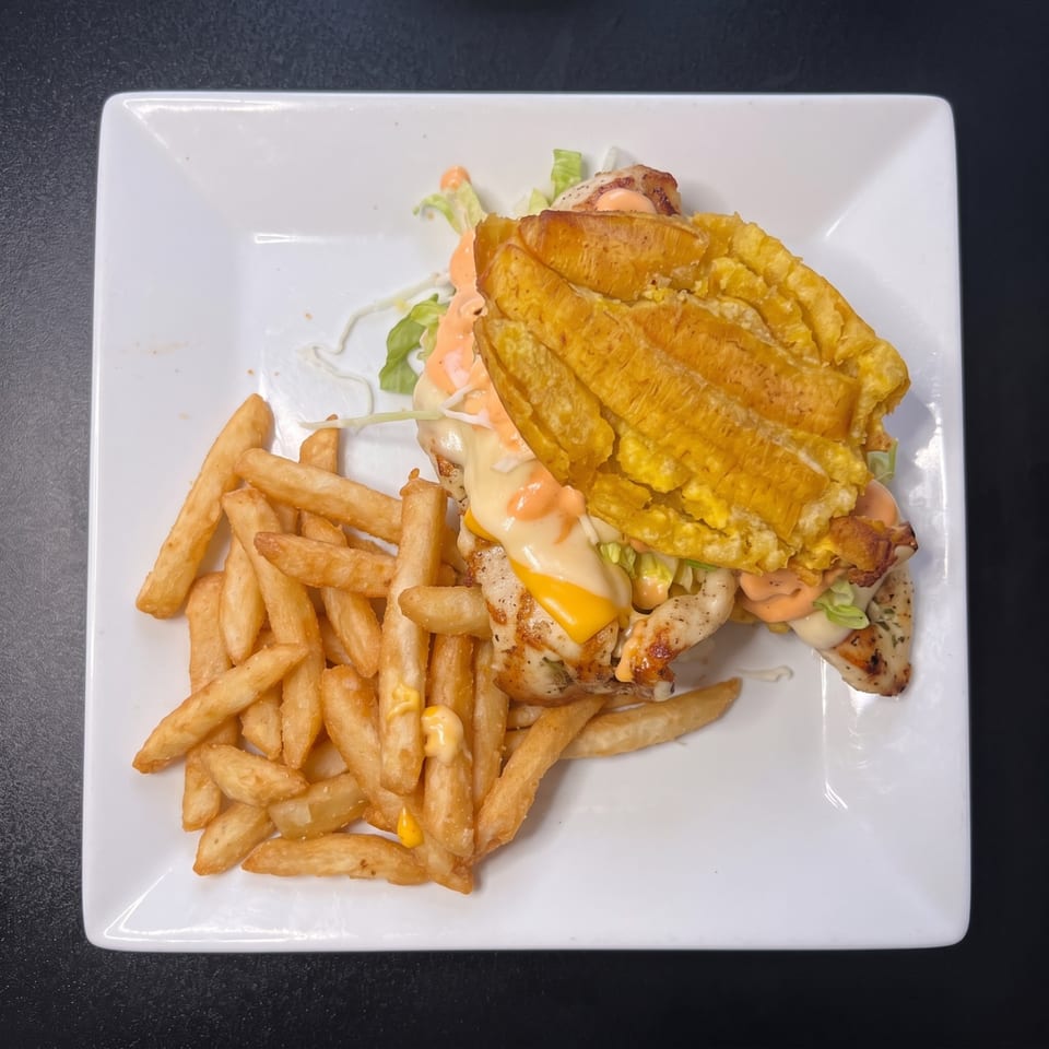 Grilled chicken sandwich with plantain buns, cheese, lettuce, and sauce, served with french fries.