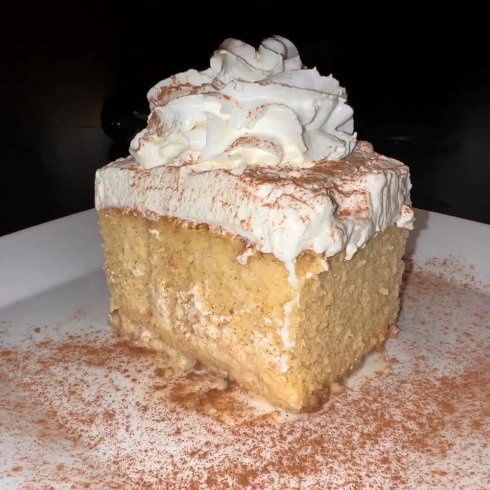 Slice of tres leches cake topped with whipped cream and cinnamon on a white plate.